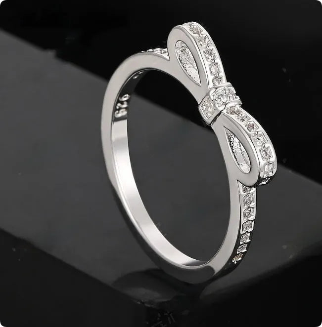 Silver bow-shaped ring set with clear rhinestone and zircon crystals on a model's hand.