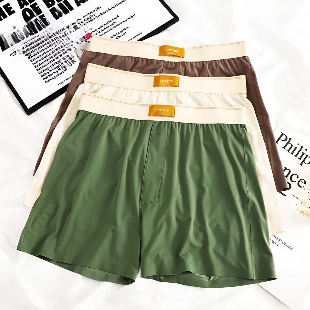 Three pairs of solid colour men's loose fit ice silk boxers laid flat, showing beige apricot, black, and dark grey.