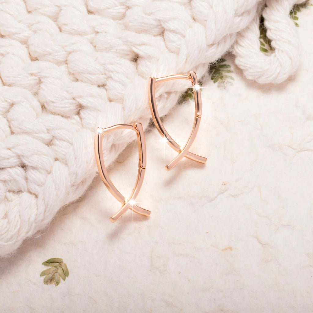 A pair of rose gold cross shaped earrings made from copper on a plain background.