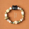 Hand-woven bracelet with jade, bodhi, and guajacwood beads, a multi-treasure cube, and a carved cat's paw charm.