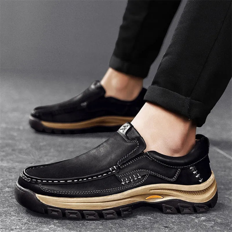 Men's black leather hiking shoes with thick rubber soles and round toe on a rocky outdoor path.