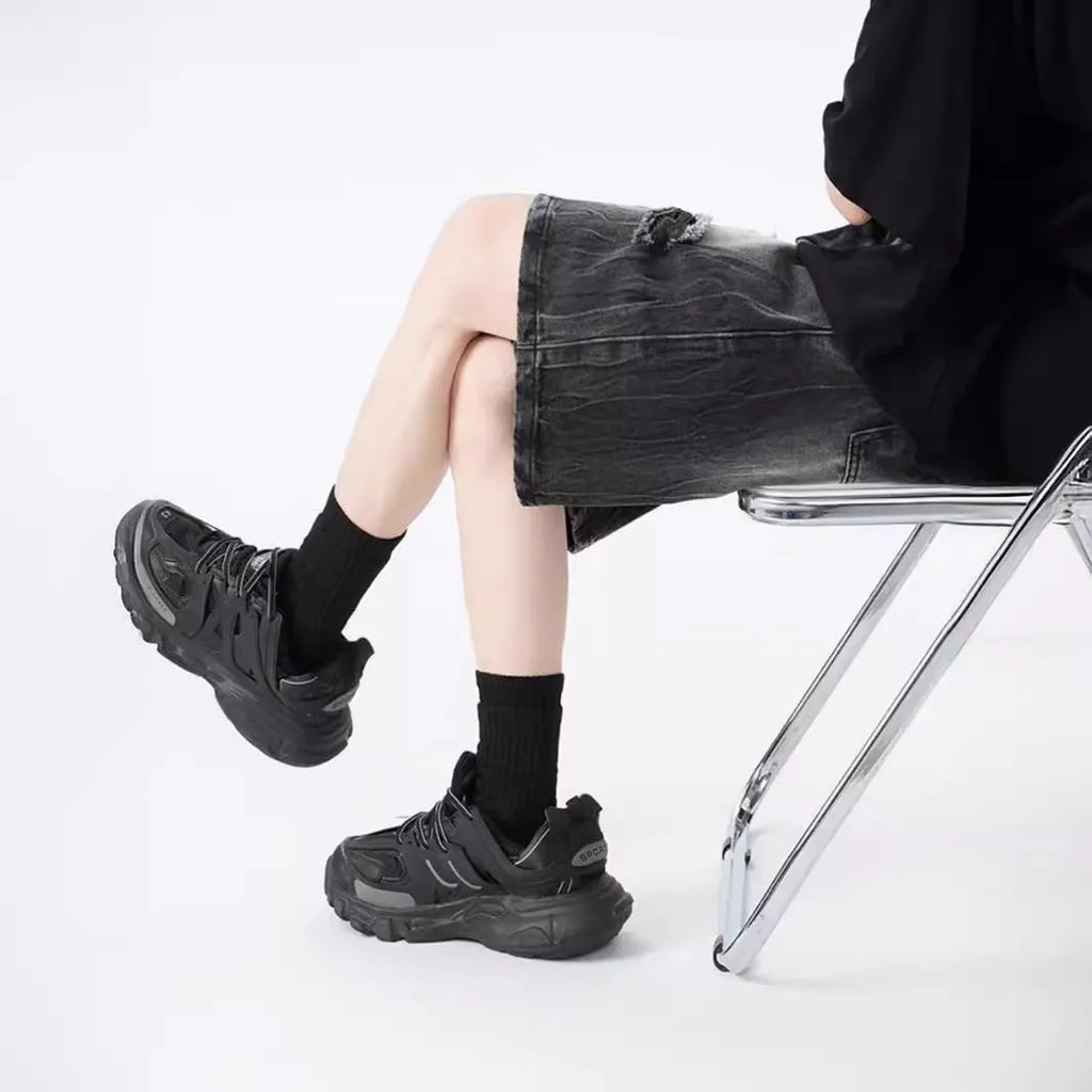 Man wearing loose-fit black denim shorts with ripped detailing and a washed vintage finish.