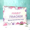 A5 habit tracking notebook in open position showing internal pages, with a choice of pink, purple, floral, or yellow and white covers.