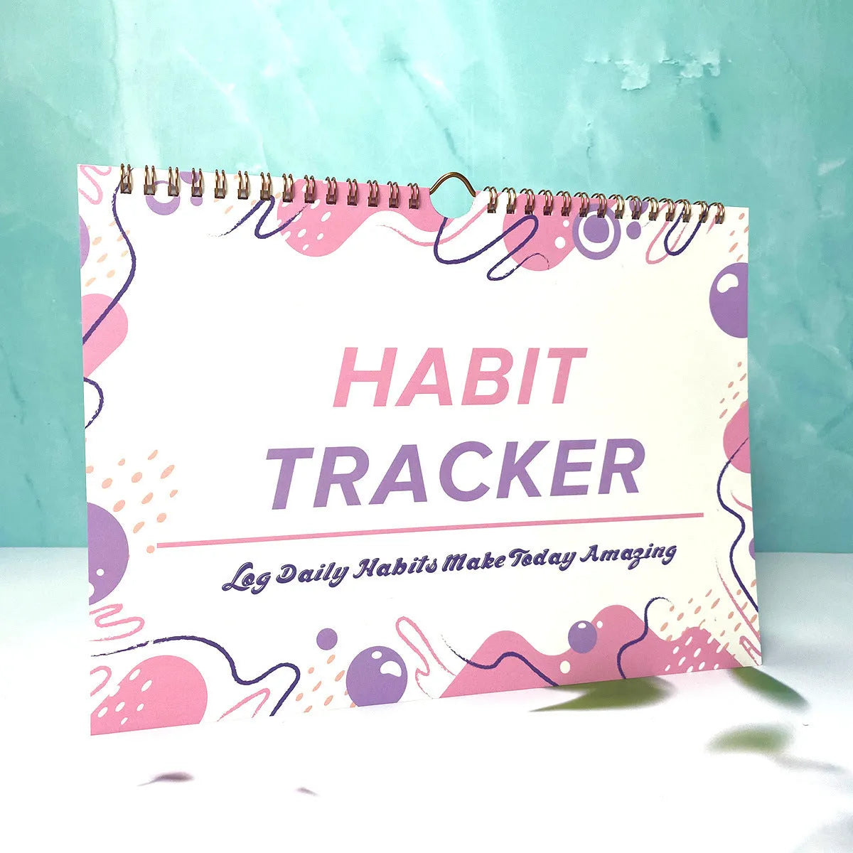 A5 habit tracking notebook in open position showing internal pages, with a choice of pink, purple, floral, or yellow and white covers.
