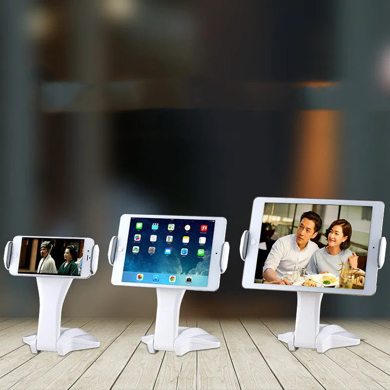 White adjustable tablet stand with a wide clip, holding a tablet on a table.