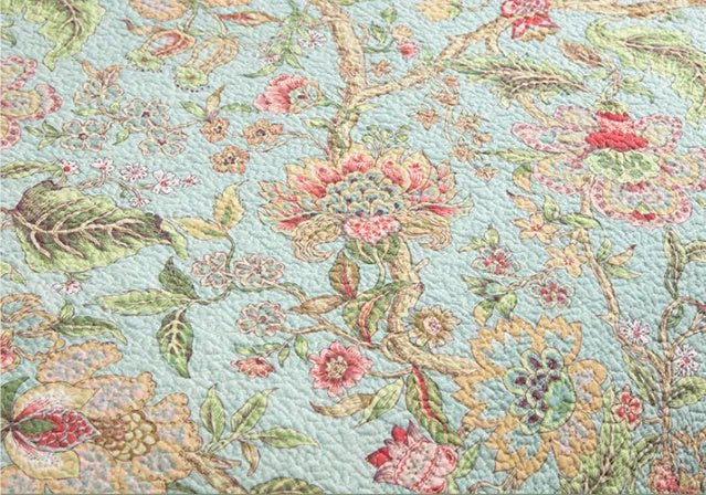 Blue American floral and bird pattern quilted cotton bedspread set laid on a bed.