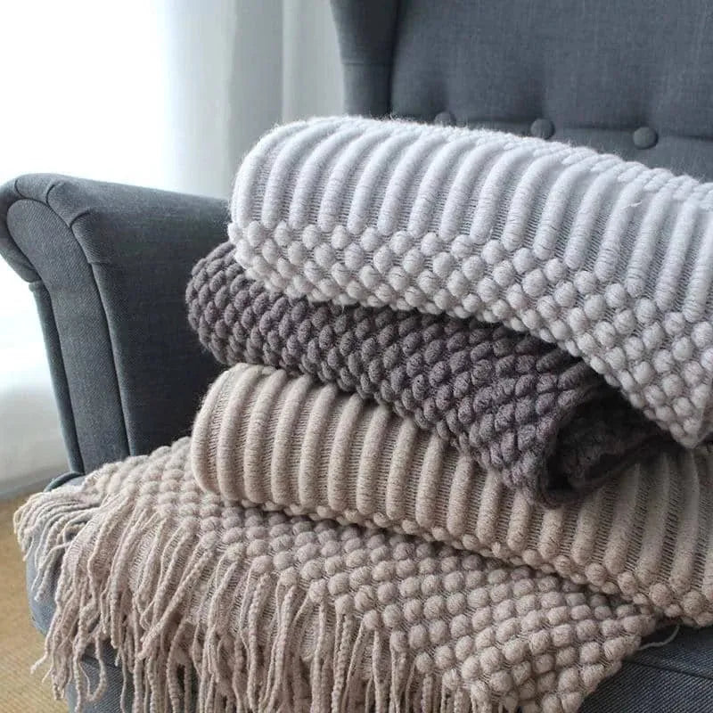 Small rectangular polyester nap blanket in neutral colour on a sofa, showing its 127 cm by 170 cm size.