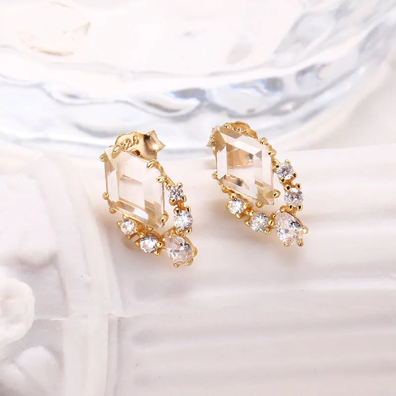 A pair of geometric shaped silver ear studs with sweet white crystal centres on a plain background.