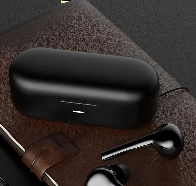 Black and white wireless in-ear Bluetooth headphones with a charging case on a table.