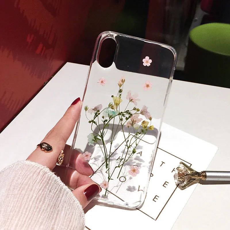 Clear TPU iPhone case with preserved pink dried flowers visible through transparent back cover