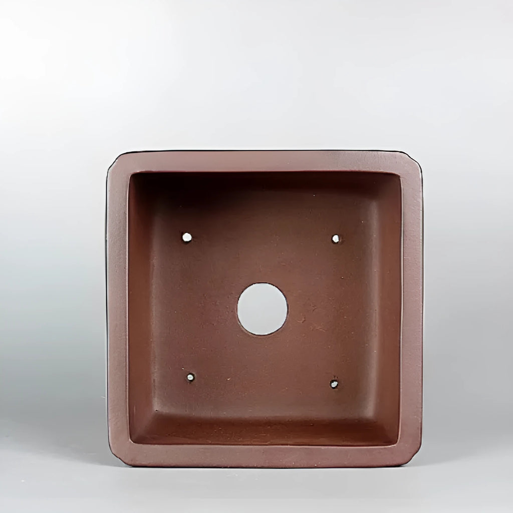 Brown handmade antique purple clay square flower pot on a windowsill.