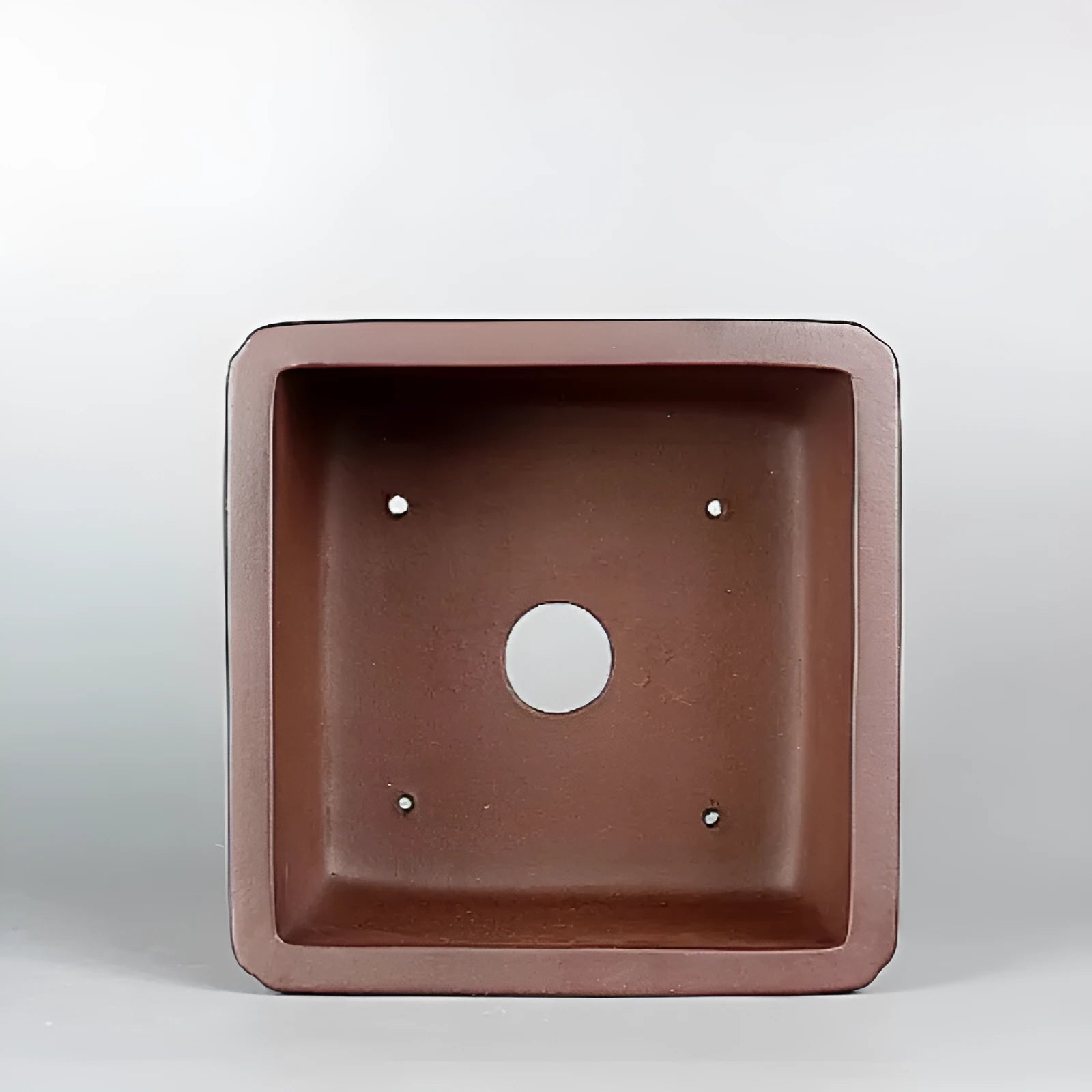Brown handmade antique purple clay square flower pot on a windowsill.