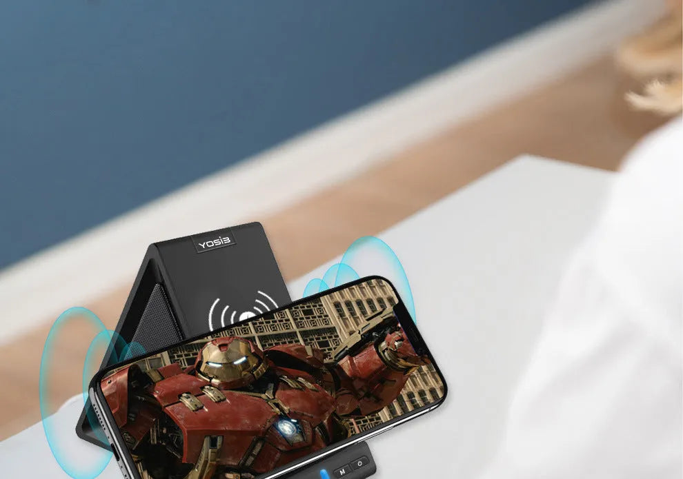 Black multifunctional Bluetooth speaker with integrated phone stand and wireless charging pad on top.