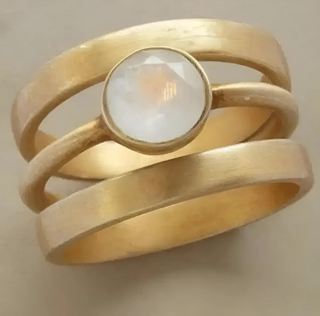 Gold-plated geometric ring with hollow band and inlaid white chalcedony stone on a grey background.