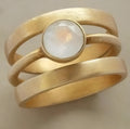 Gold-plated geometric ring with hollow band and inlaid white chalcedony stone on a grey background.