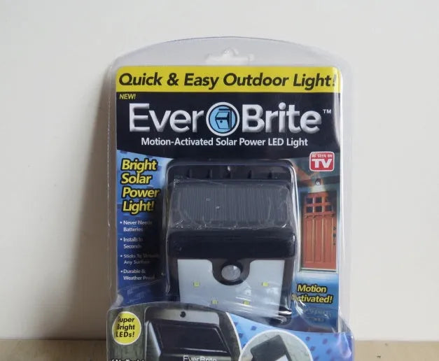 Grey solar-powered outdoor security light with four LED panels and a motion sensor mounted on a wall.