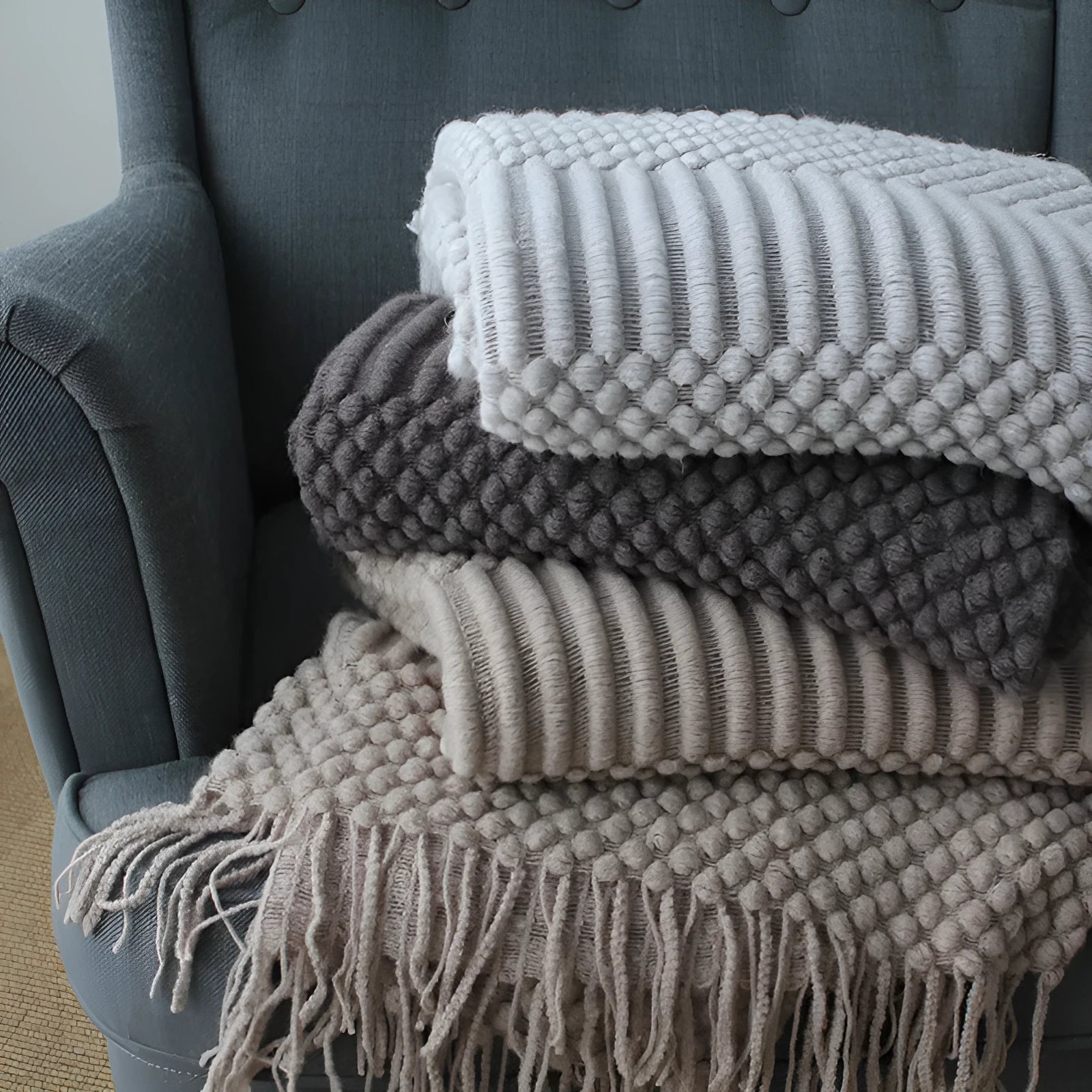 Small rectangular polyester nap blanket in neutral colour on a sofa, showing its 127 cm by 170 cm size.