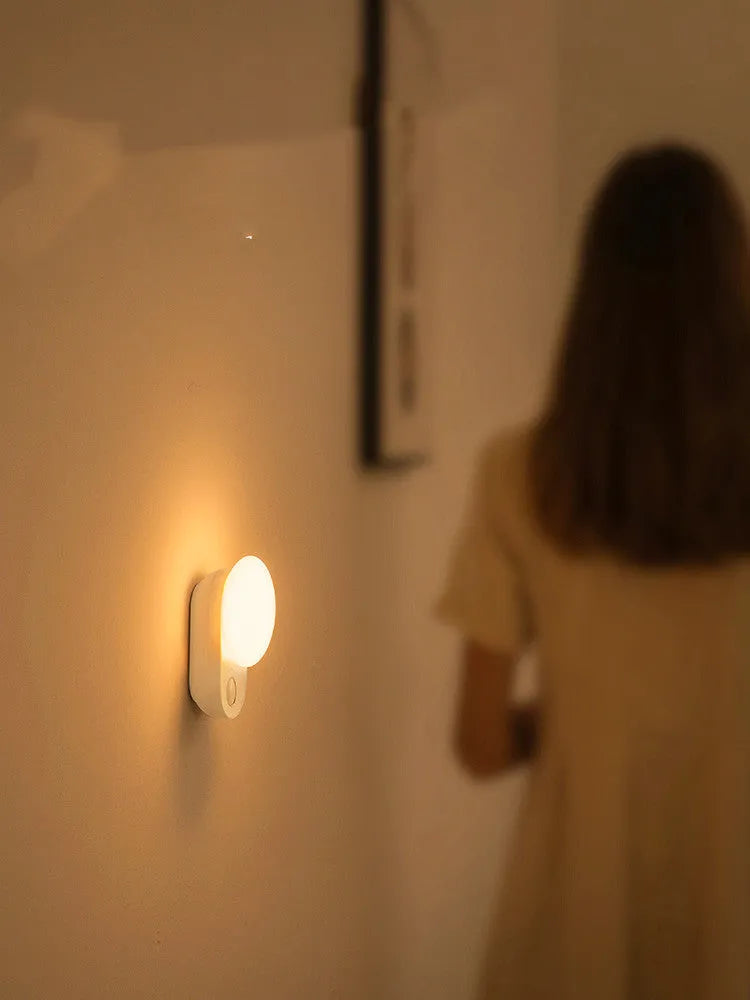 White Baseus rechargeable sensor night light with motion detection on a bedside table.
