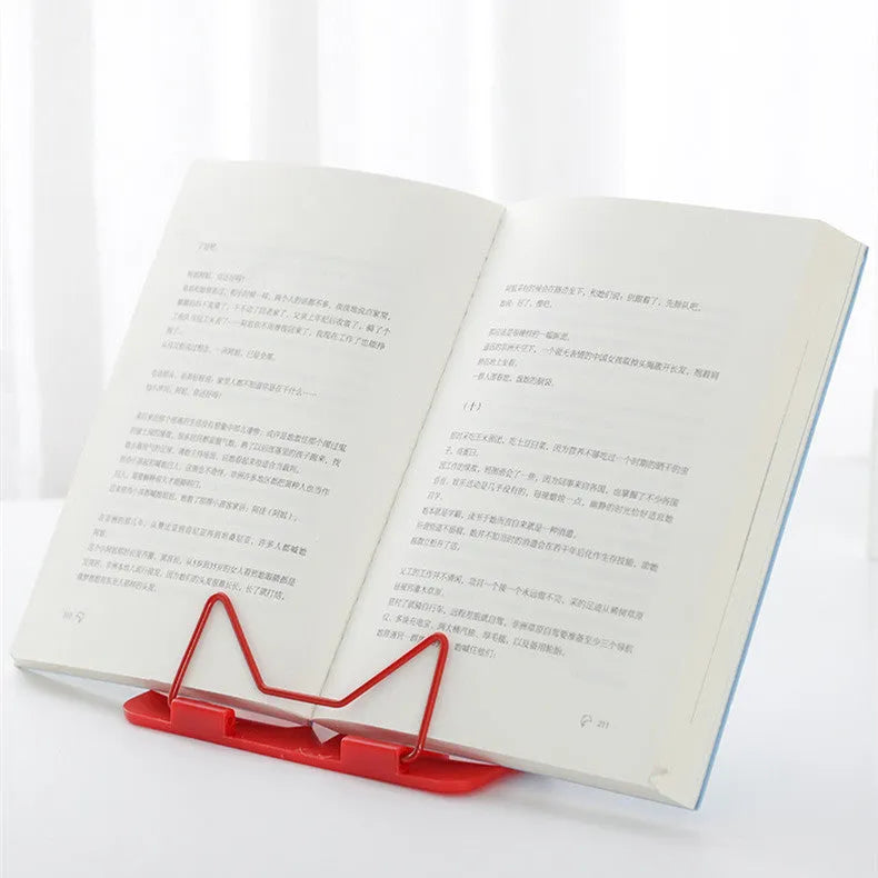 A red metal and plastic reading frame holding a book upright on a desk.