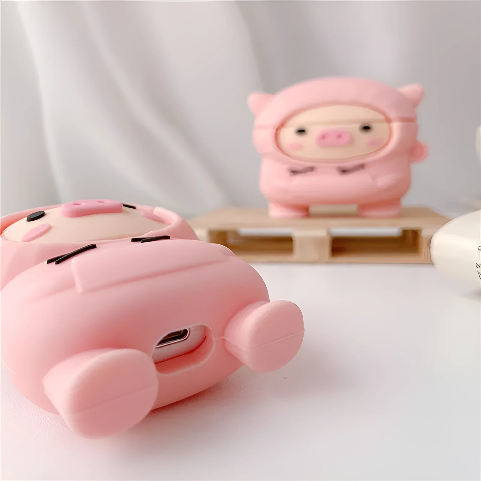 Pink silicone AirPods case cover with cartoon pig design, showing flip-style opening and hook attachment