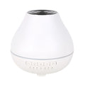 Round white Bluetooth humidifier and aroma diffuser with night light on a table.