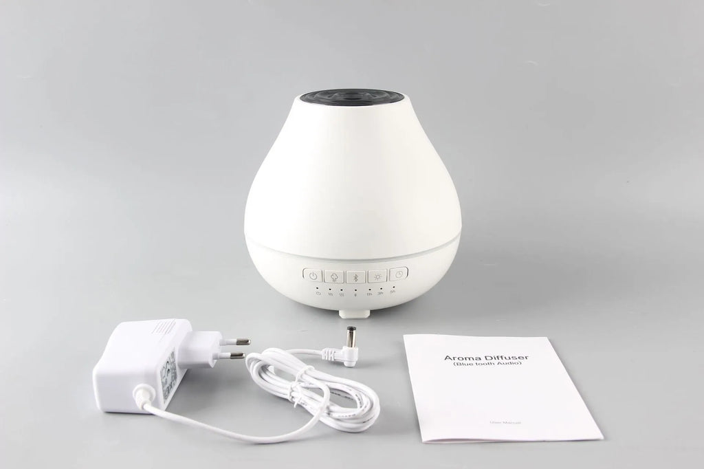 Round white Bluetooth humidifier and aroma diffuser with night light on a table.
