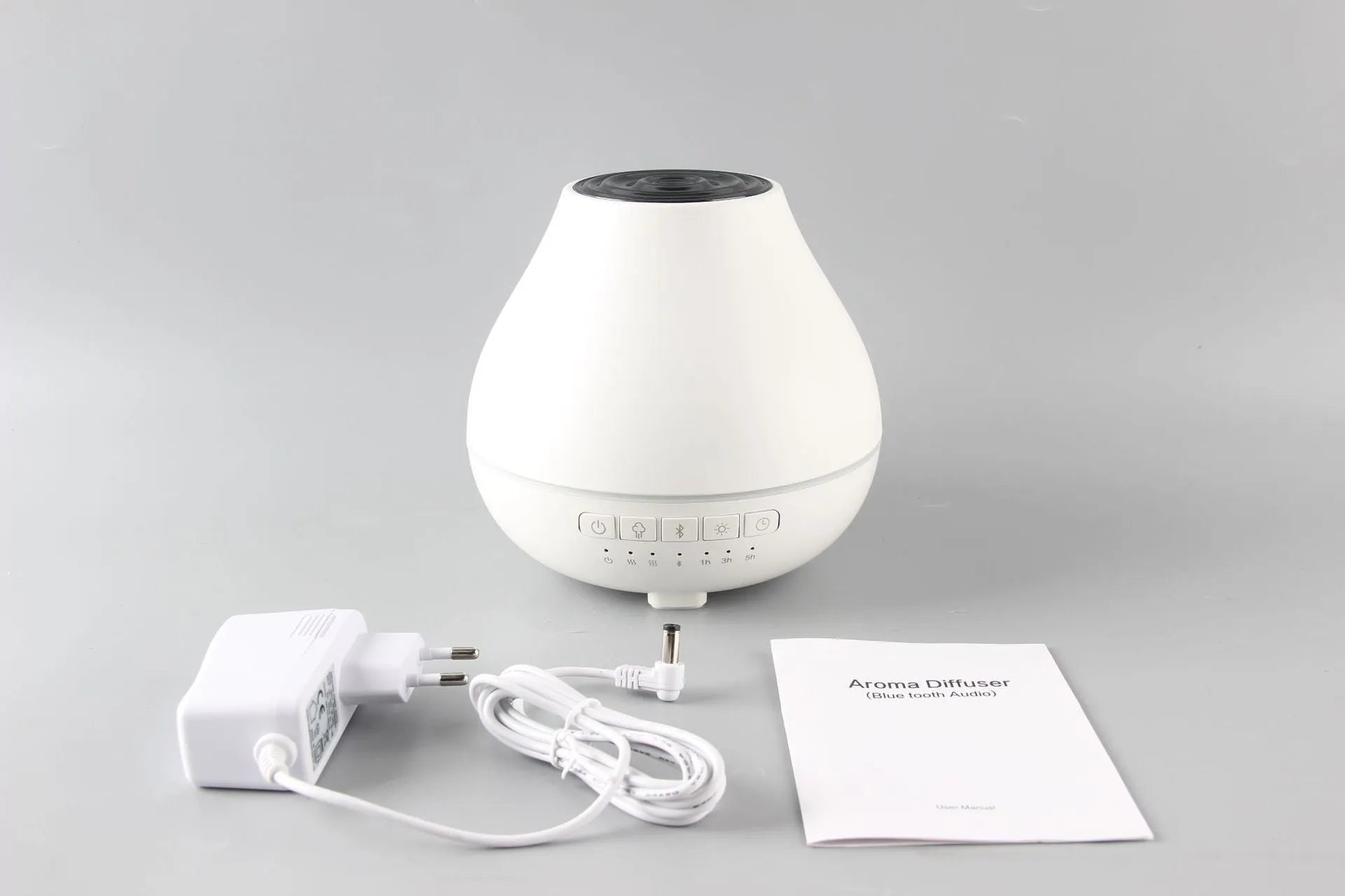 Round white Bluetooth humidifier and aroma diffuser with night light on a table.