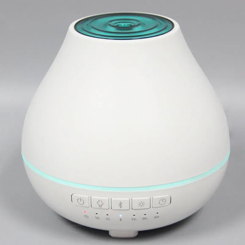 Round white Bluetooth humidifier and aroma diffuser with night light on a table.