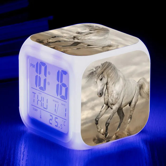 Small square cartoon-style LED alarm clock showing digital time on a plexiglass display.