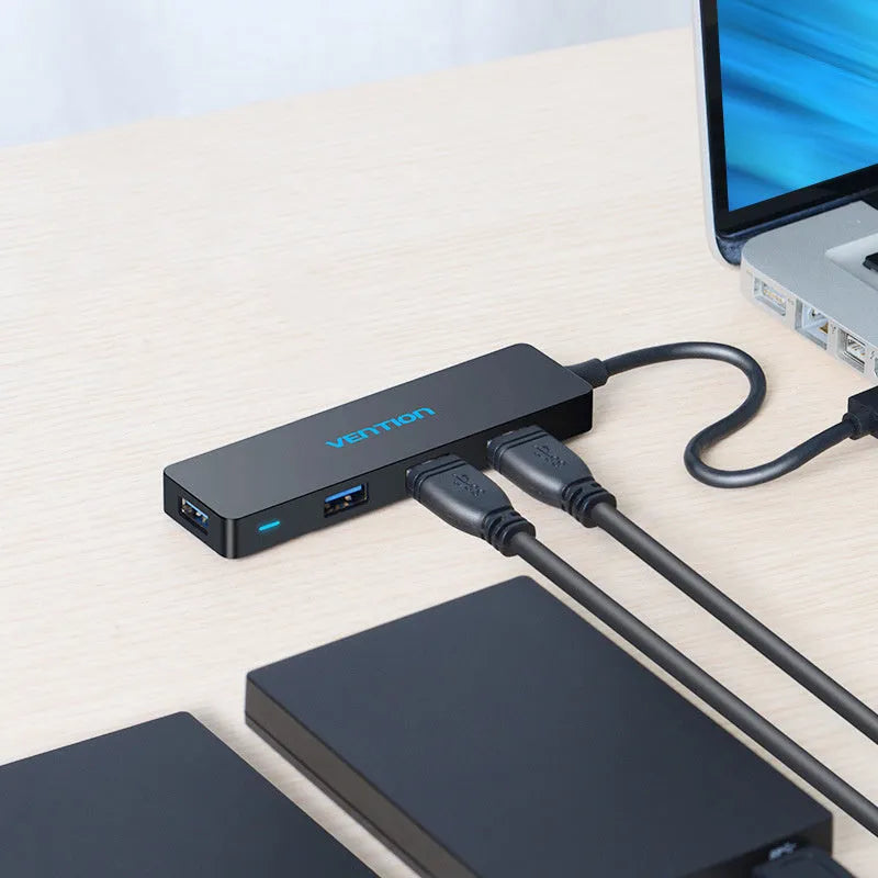 Black USB 3.0 hub with four ports and a short braided cable on a desk.