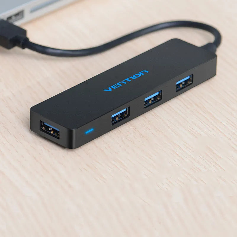 Black four-port USB 3.0 hub with a short 15cm cable on a desk.