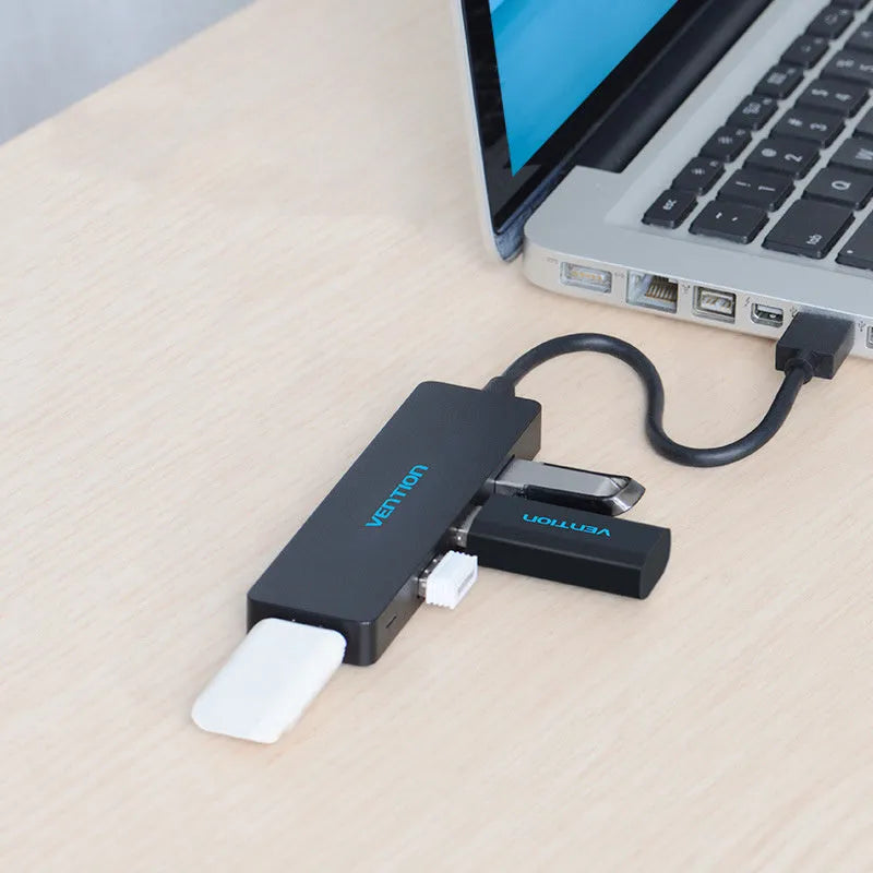 Black USB 3.0 hub with four ports and a short braided cable on a desk.