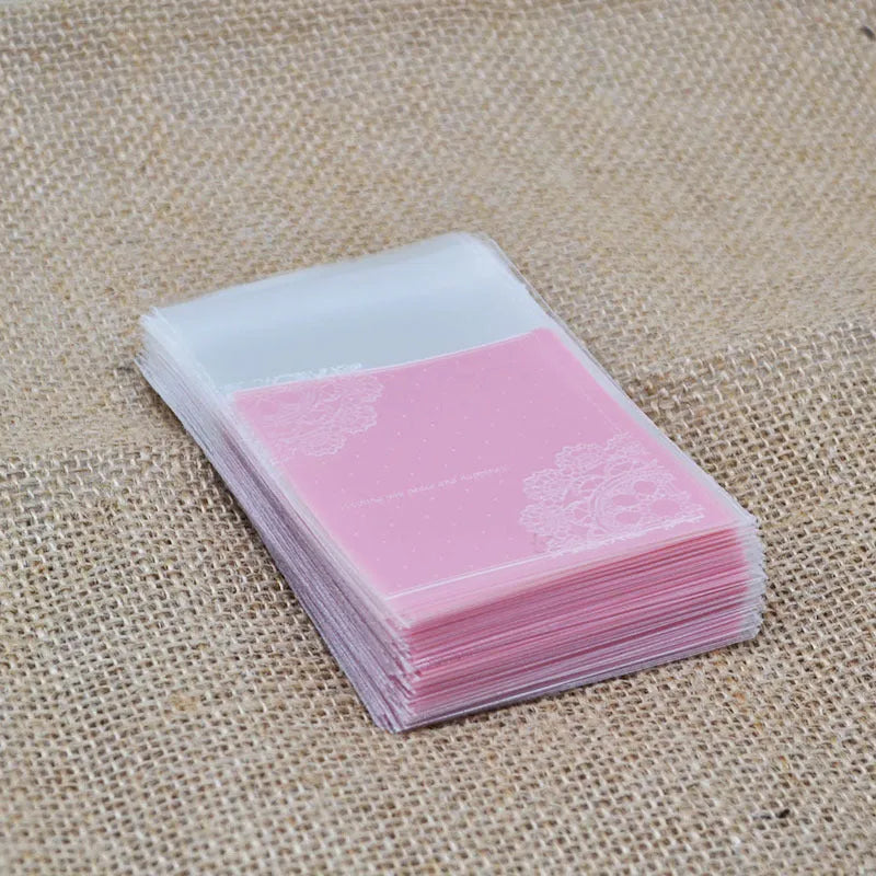 Clear pink self-adhesive plastic packaging bag with flap, shown next to a bar of soap.