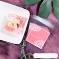 Clear pink self-adhesive plastic packaging bag with flap, shown next to a bar of soap.