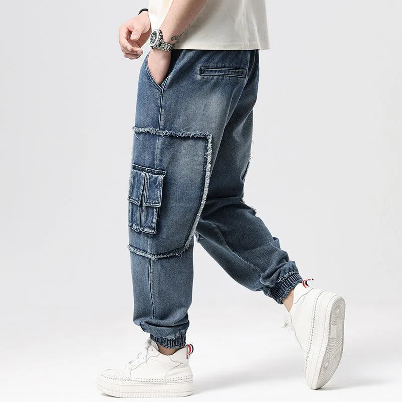 Man wearing loose-fit blue denim hip hop trousers with multiple pockets and a straight leg.