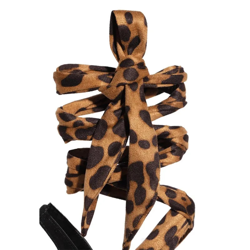 Light brown leopard print Roman-style high heel sandals with cross straps on a wooden floor.