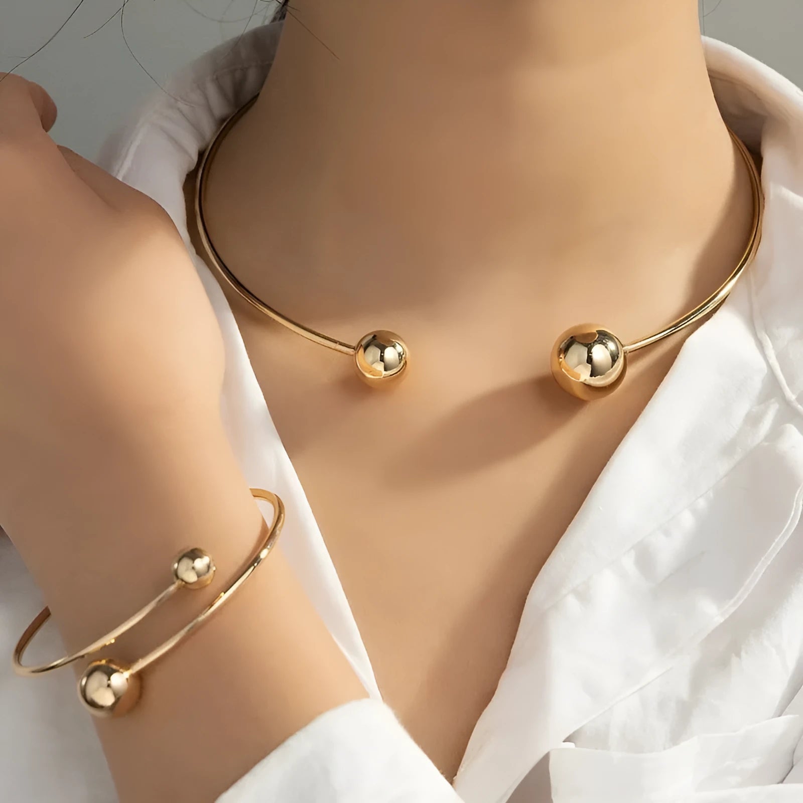 Gold dislocation ball open-end thin bangle bracelet with matching necklace on a flat surface