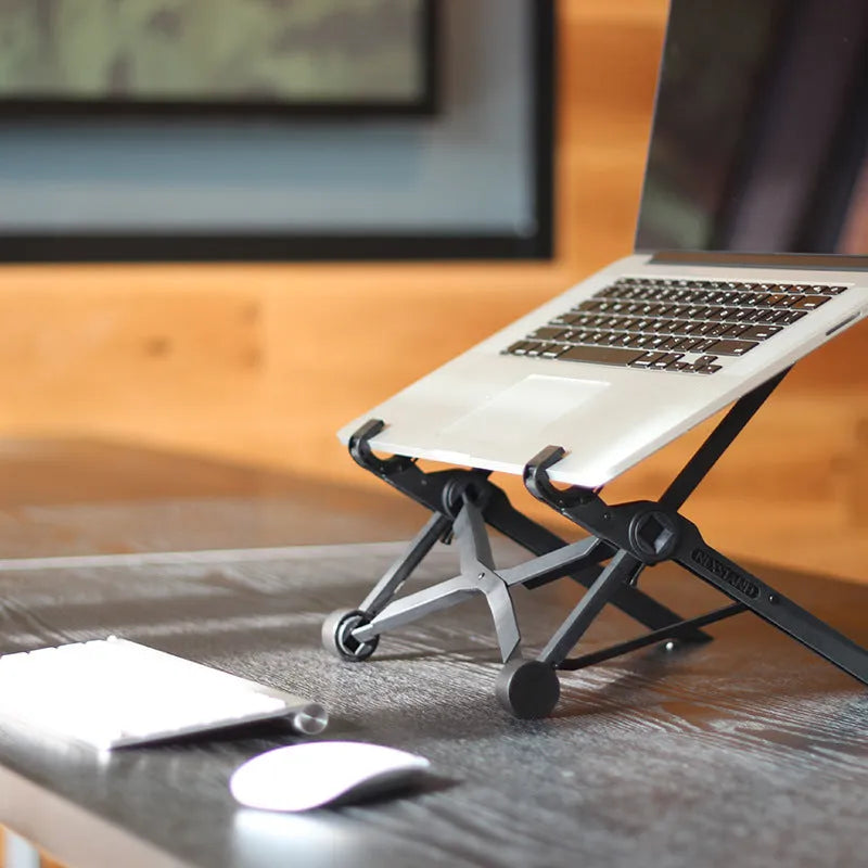 Black folding portable laptop stand made of reinforced nylon, shown folded to its compact size.