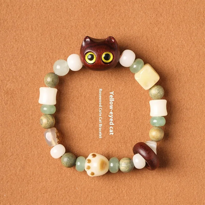 Hand-woven bracelet with jade, bodhi, and guajacwood beads, a multi-treasure cube, and a carved cat's paw charm.