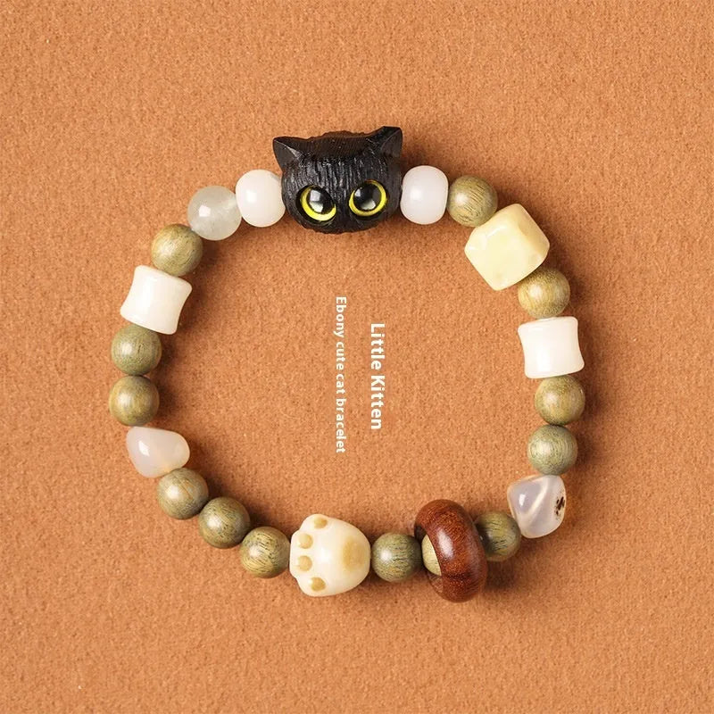 Hand-woven bracelet with jade, bodhi, and guajacwood beads, a multi-treasure cube, and a carved cat's paw charm.
