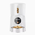 Black automatic pet feeder with digital display and stainless steel bowl on a kitchen floor.