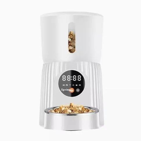 Black automatic pet feeder with digital display and stainless steel bowl on a kitchen floor.