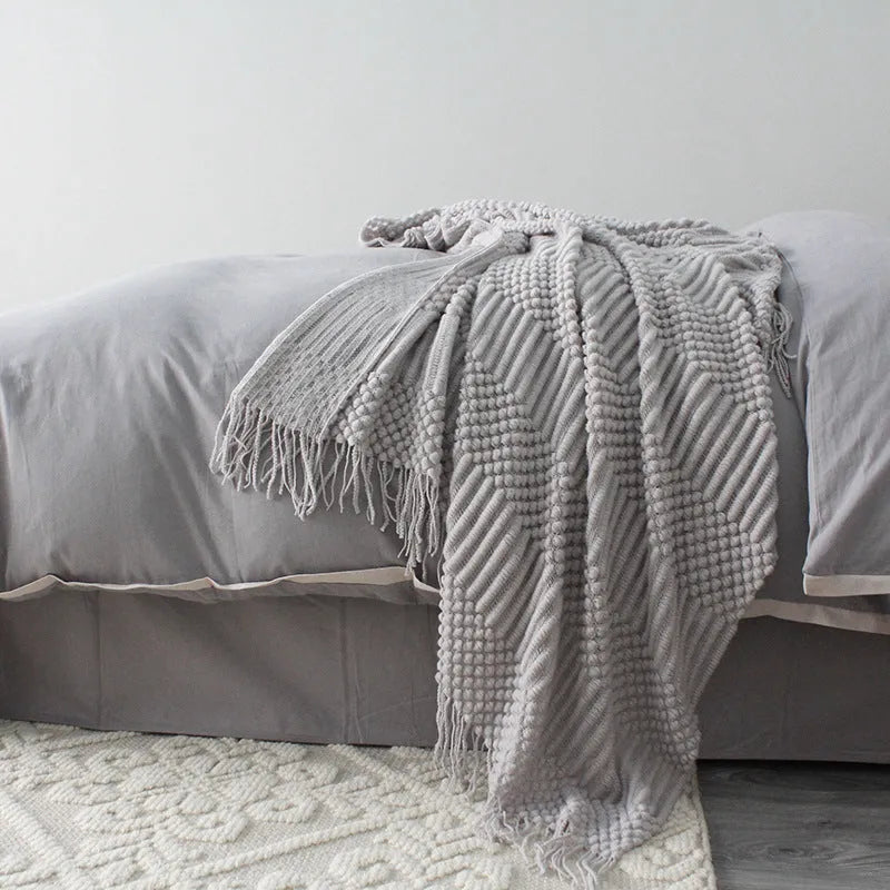 Small rectangular polyester nap blanket in neutral colour on a sofa, showing its 127 cm by 170 cm size.