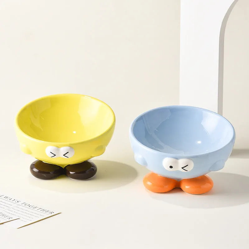 Blue and yellow ceramic slanted pet food bowls with animal face expressions for cervical spine support.