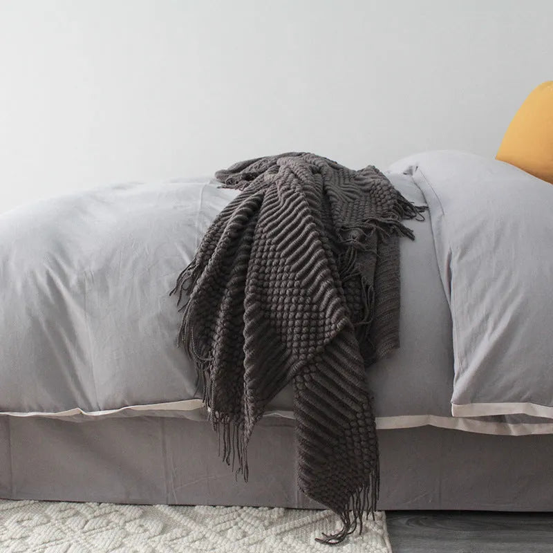 Small rectangular polyester nap blanket in neutral colour on a sofa, showing its 127 cm by 170 cm size.