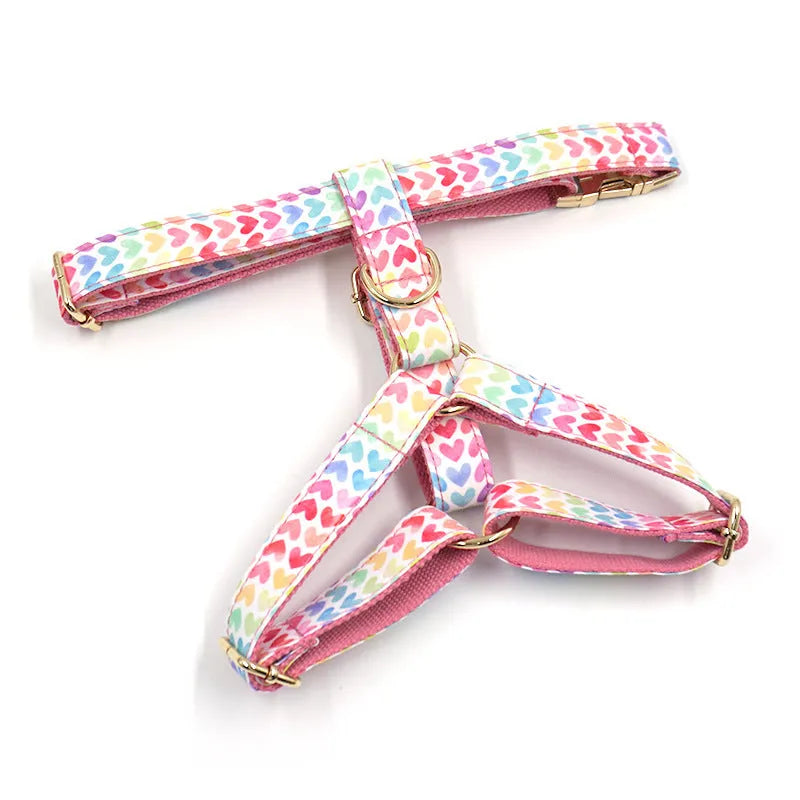 Pink dog harness with colourful heart-shaped stones and a gold-coloured buckle on a white background.