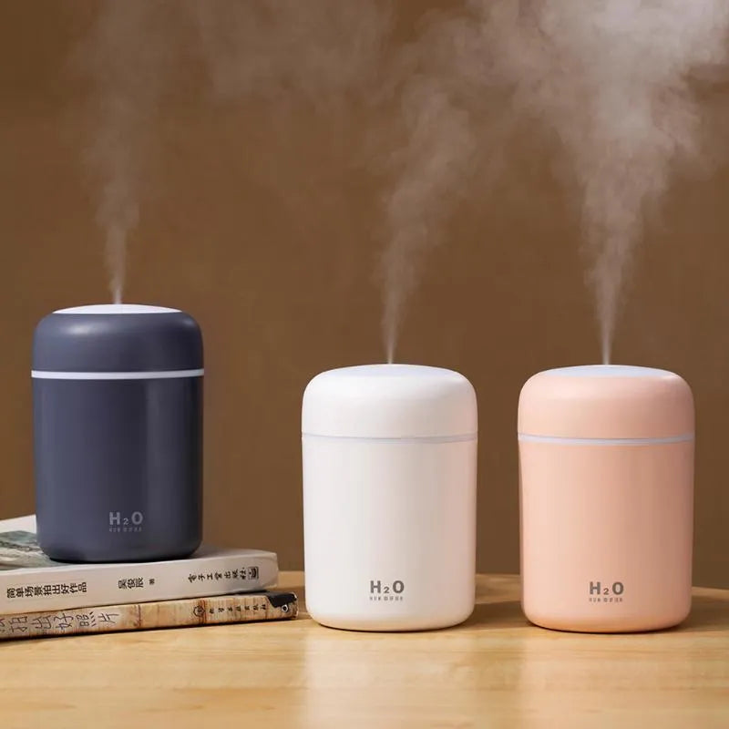 Pink USB desktop humidifier with LED lights emitting mist on a wooden desk