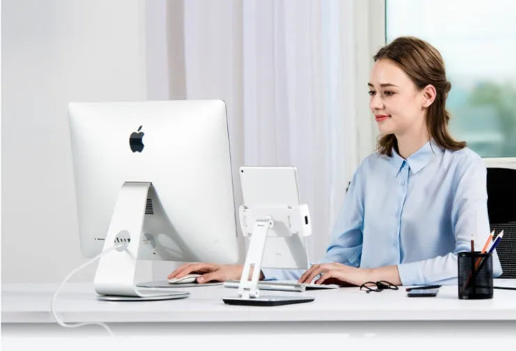 Silver foldable aluminium phone tablet stand with 360-degree rotating bracket on a desktop.