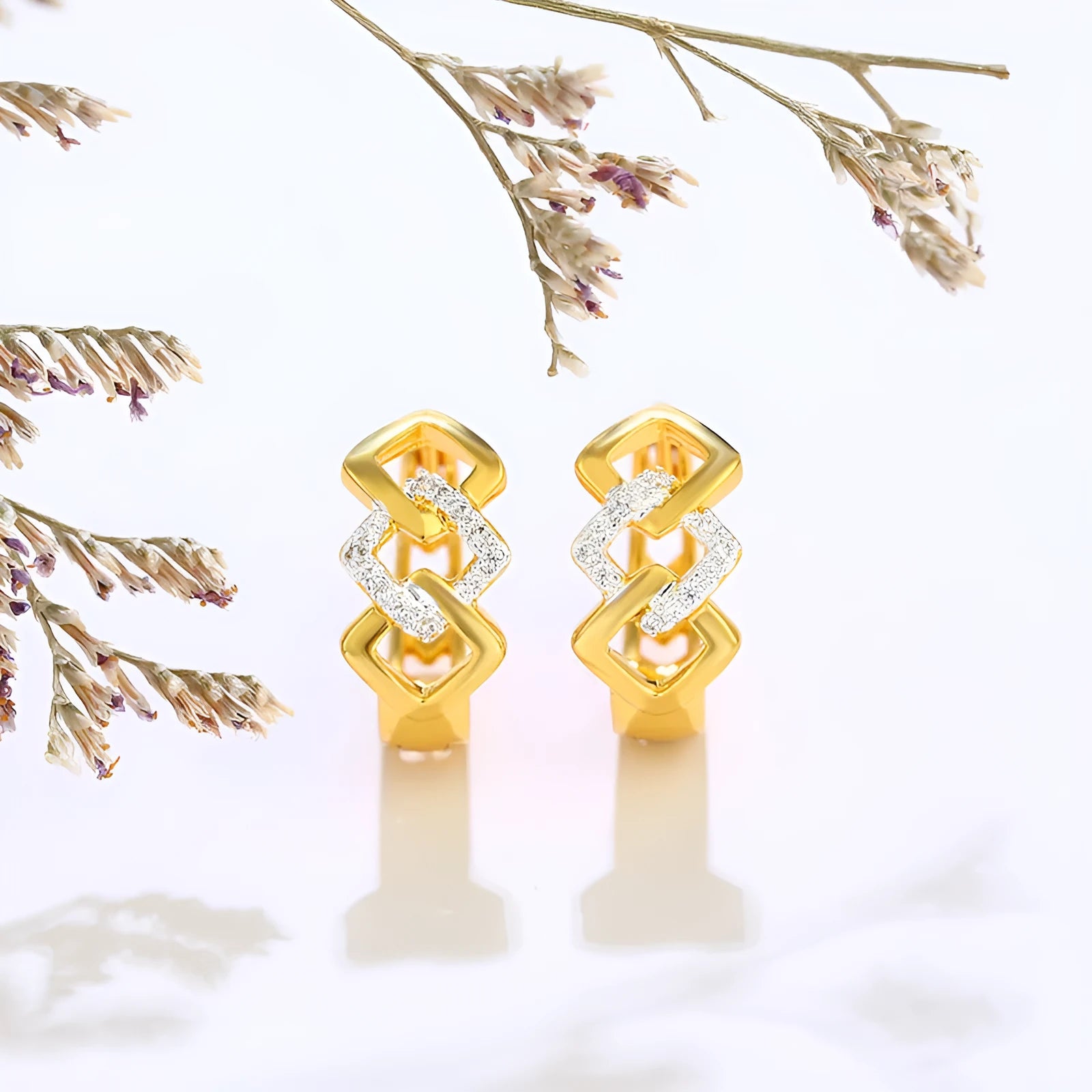 A pair of gold-coloured geometric drop earrings with a hollow out design on a plain background.