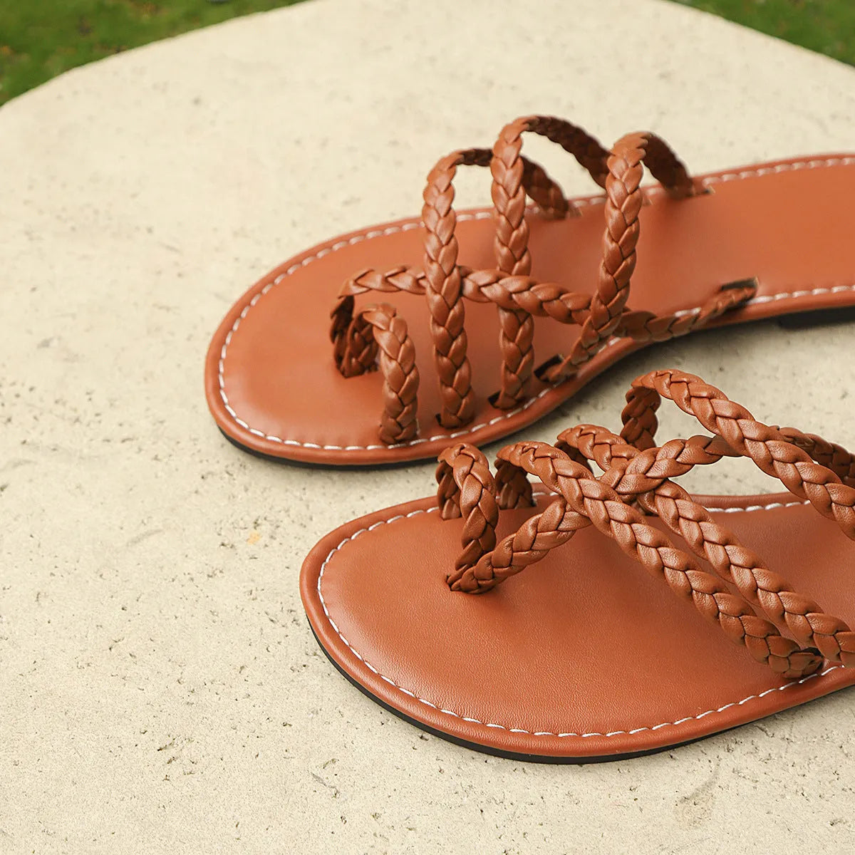Women's woven clip-toe sandals in black, showing Roman-style straps and a flat rubber sole.